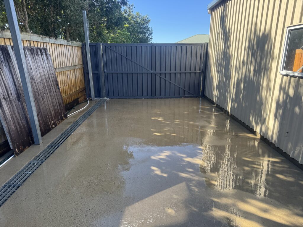 The same concrete area beside a shed after rinsing, with the surface still wet.