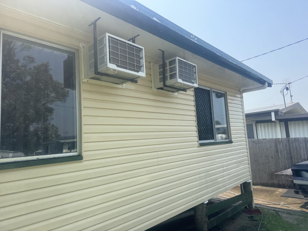 Clean eaves and cream weatherboard walls around two window air conditioners in North Mackay