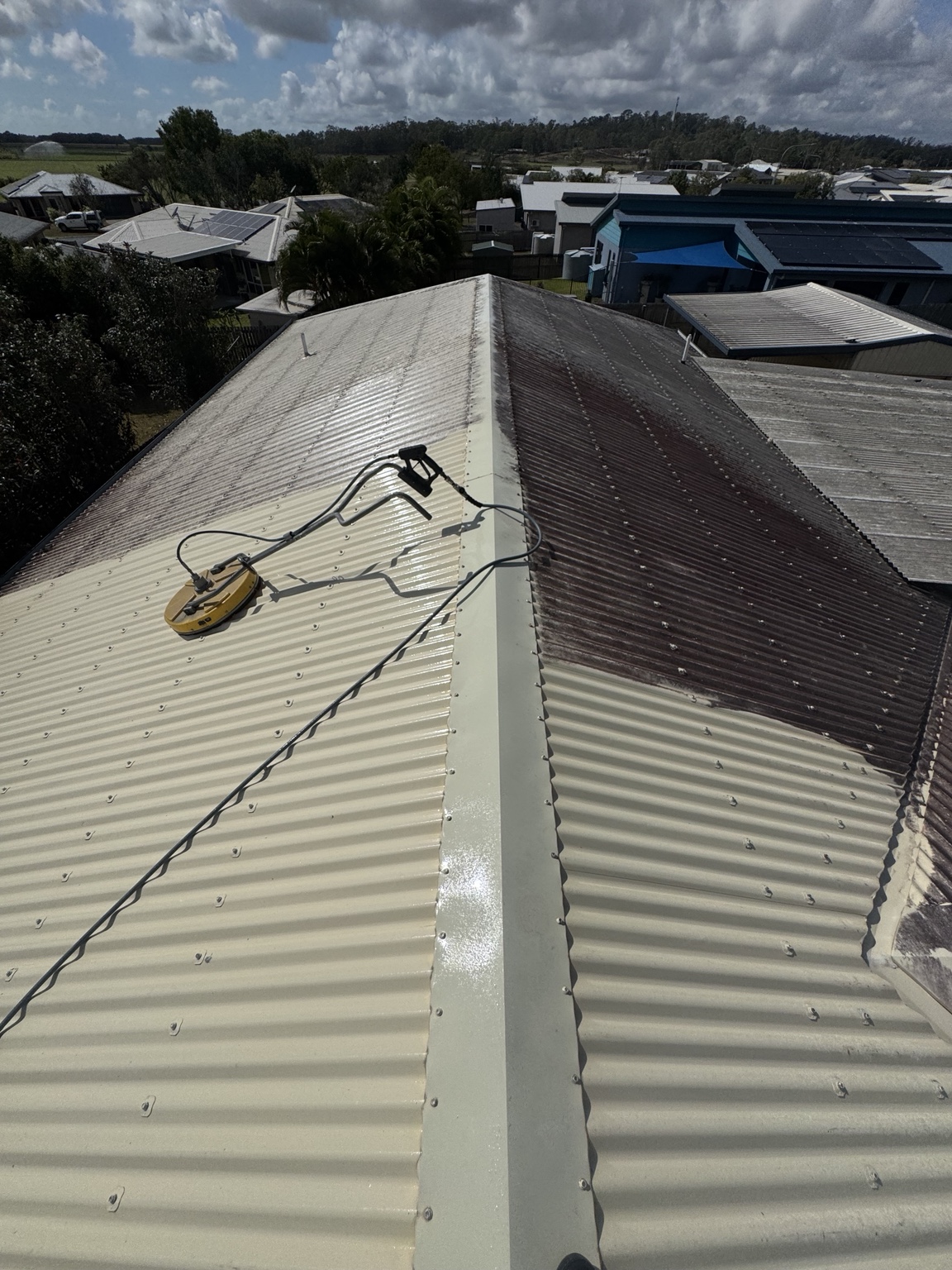 Surface cleaner beside cleaned and darkened corrugated roof sections in Walkerston